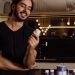 A smiling man in a kitchen holds a bottle of supplements, showcasing health and wellness.